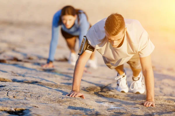 Jovem casal fazendo flexões na praia do oceano — Fotografia de Stock