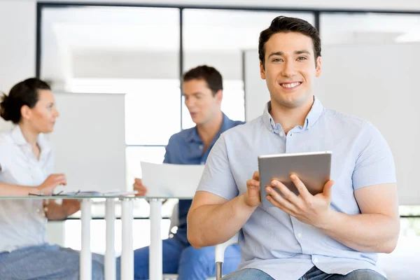 Joven hombre de negocios guapo usando su touchpad sentado en la oficina —  Fotos de Stock