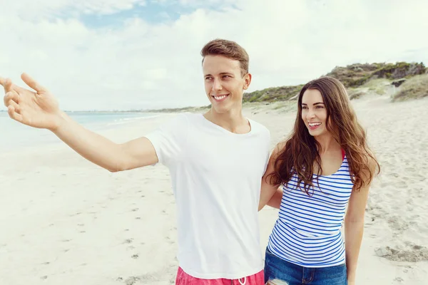 Gelukkige jonge man en vrouw paar samen wandelen op een strand — Stockfoto