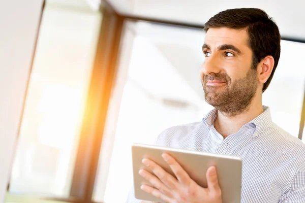 Joven hombre de negocios guapo usando su touchpad de pie en la oficina — Foto de Stock