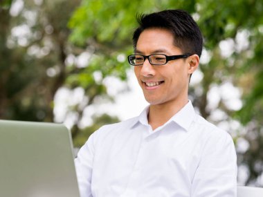 Genç işadamı açık havada otururken dizüstü bilgisayar kullanarak