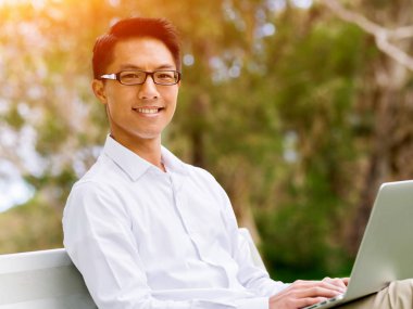 Genç işadamı açık havada otururken dizüstü bilgisayar kullanarak