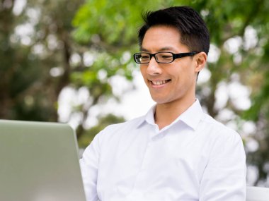 Genç işadamı açık havada otururken dizüstü bilgisayar kullanarak