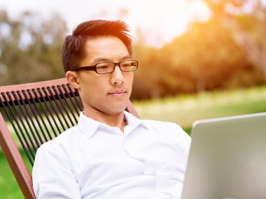 Genç işadamı açık havada otururken dizüstü bilgisayar kullanarak