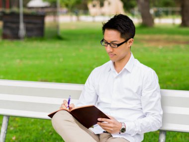 Bankta oturan ve Not Defteri'nde yazma çekici düşünceli işadamı