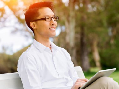 Genç işadamı açık havada otururken dizüstü bilgisayar kullanarak