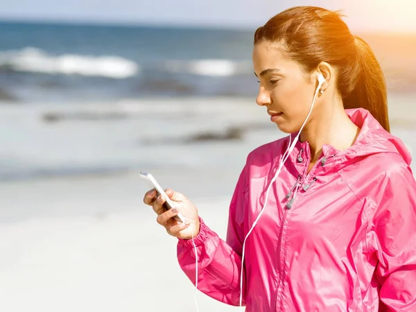 Sporty woman with earphones on the sea coast — Stock Photo, Image