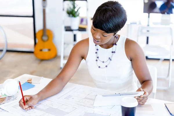 Young woman sitting at a desk in an office and working on blueprint — Stock Photo, Image