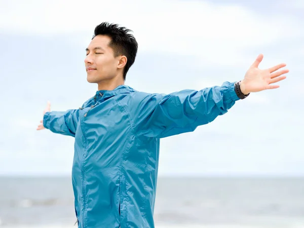 Ung man med utsträckta armar på stranden — Stockfoto