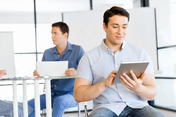 Joven hombre de negocios guapo usando su touchpad sentado en la oficina —  Fotos de Stock