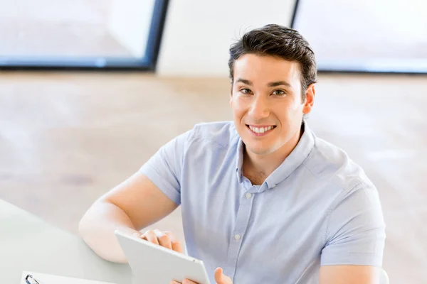 Young handsome businessman using his touchpad sitting in office — Stock Photo, Image