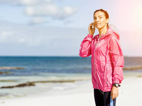 Sporty woman with earphones on the sea coast — Stock Photo, Image