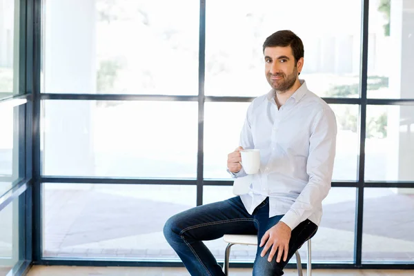 Junger Geschäftsmann sitzt auf einem Hocker im Büro — Stockfoto