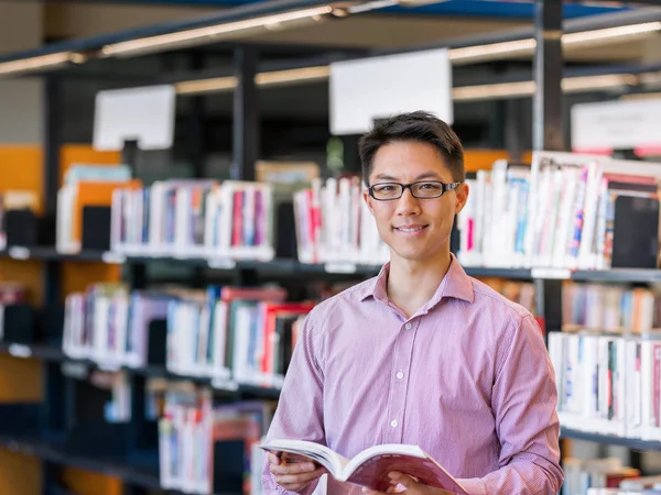 Feliz estudiante masculino sosteniendo libros en la biblioteca —  Fotos de Stock
