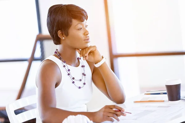 Bir ofiste bir masada oturan ve plan üzerinde çalışan genç kadın — Stok fotoğraf