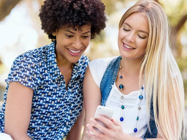 Two women friends in park with mobile phone — Stock Photo, Image
