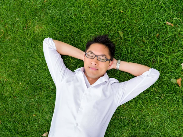 Ppretty genç adam beyaz gömlekli bir çim üzerinde rahatlatıcı