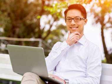 Genç işadamı açık havada otururken dizüstü bilgisayar kullanarak