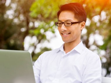 Genç işadamı açık havada otururken dizüstü bilgisayar kullanarak