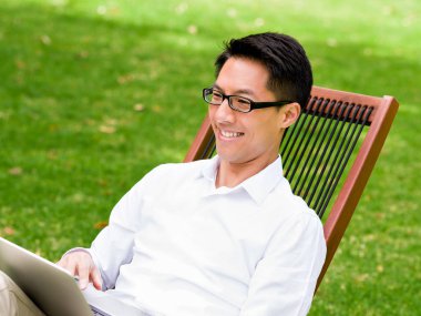 Genç işadamı açık havada otururken dizüstü bilgisayar kullanarak