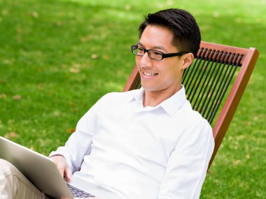 Genç işadamı açık havada otururken dizüstü bilgisayar kullanarak