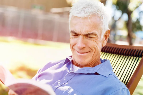 Homem sênior sentado no parque enquanto lê o livro — Fotografia de Stock