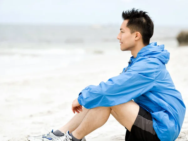 Mladý muž sedí na pláži v sportswear — Stock fotografie