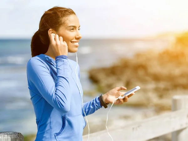 Sporty woman with earphones on the sea coast — Stock Photo, Image