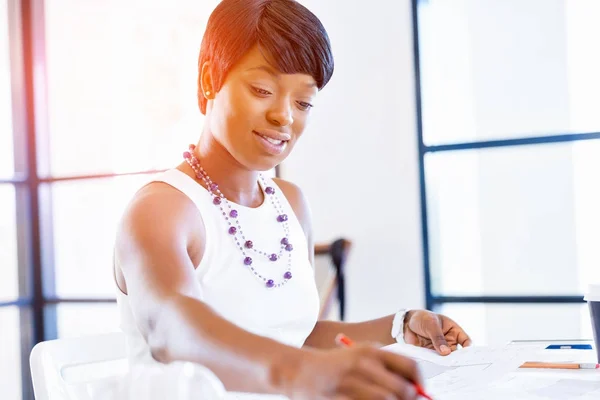 Young woman sitting at a desk in an office and working on blueprint — Stock Photo, Image