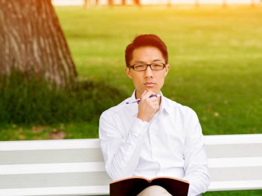 Bankta oturan ve Not Defteri'nde yazma çekici düşünceli işadamı