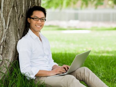 Genç işadamı açık havada otururken dizüstü bilgisayar kullanarak