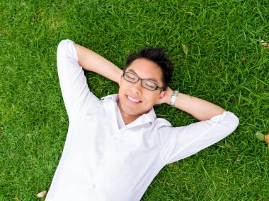 Ppretty genç adam beyaz gömlekli bir çim üzerinde rahatlatıcı