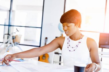 Bir ofiste bir masada oturan ve plan üzerinde çalışan genç kadın