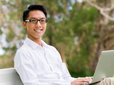 Genç işadamı açık havada otururken dizüstü bilgisayar kullanarak