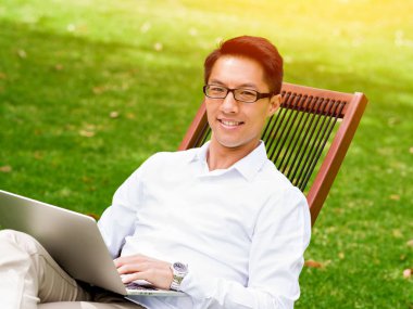 Genç işadamı açık havada otururken dizüstü bilgisayar kullanarak