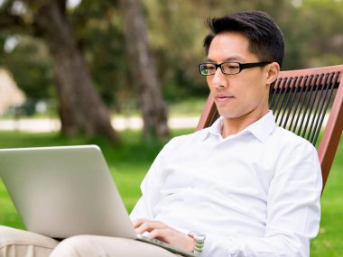 Genç işadamı açık havada otururken dizüstü bilgisayar kullanarak