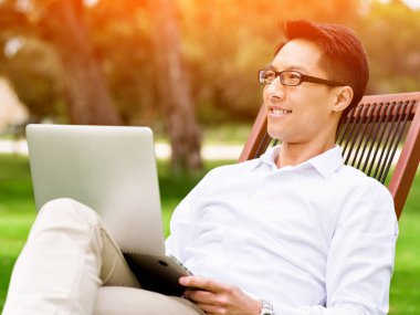 Genç işadamı açık havada otururken dizüstü bilgisayar kullanarak