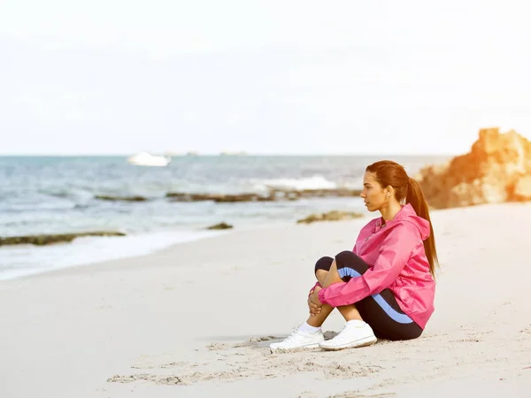 Jonge vrouw zittend op het strand in sportkleding — Stockfoto