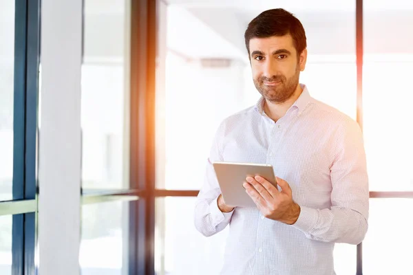 Jeune homme d'affaires beau utilisant son pavé tactile debout dans le bureau — Photo