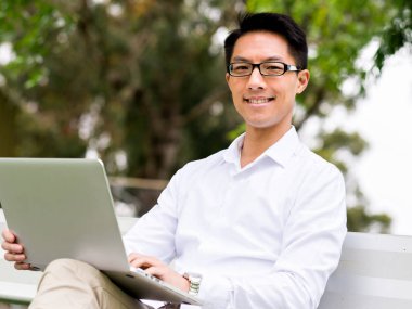 Genç işadamı açık havada otururken dizüstü bilgisayar kullanarak