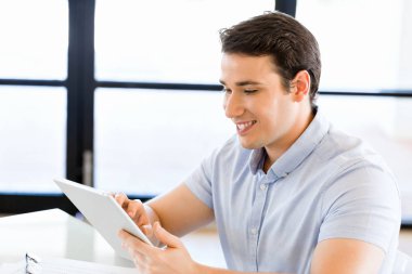 Genç yakışıklı işadamı ofisinde oturup onun touchpad kullanarak