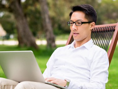 Genç işadamı açık havada otururken dizüstü bilgisayar kullanarak