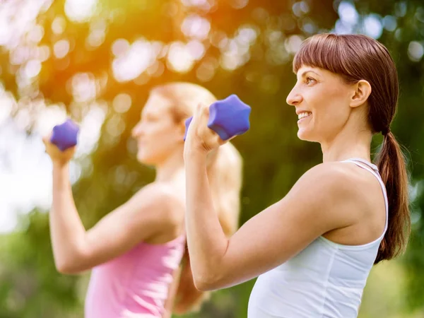 Retrato de mujeres alegres en ropa de fitness haciendo ejercicio con mancuerna — Foto de Stock