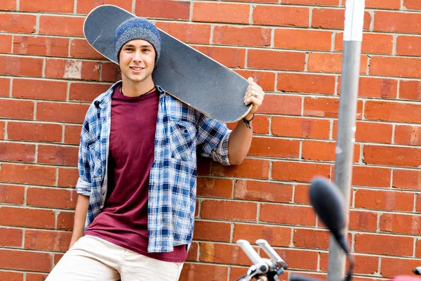 Adolescente con monopatín de pie junto a la pared — Foto de Stock