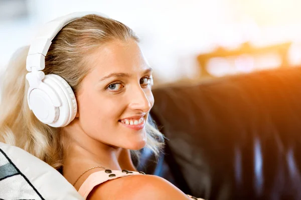 Молодая улыбающаяся женщина с наушниками отдыхает на диване, слушая музыку онлайн с помощью смартфона — стоковое фото