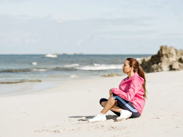 Ung kvinna sitter vid stranden i sportkläder — Stockfoto