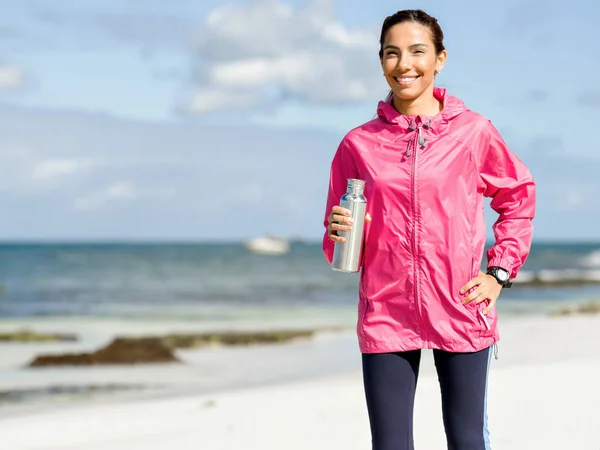 Hermosa chica en ropa deportiva beber agua después del entrenamiento en la playa —  Fotos de Stock