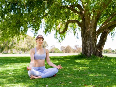 Genç kadın parkta yoga yapıyor.
