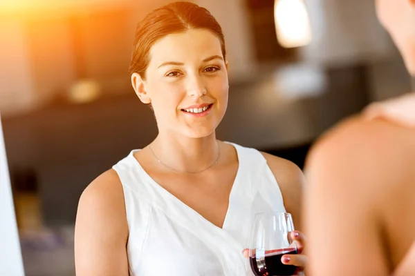 Ung kvinna med hennes vän hålla ett glas vin inomhus — Stockfoto