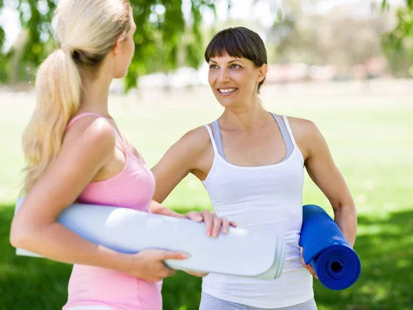 Dos mujeres jóvenes con una alfombra de gimnasio charlando en el parque — Foto de Stock